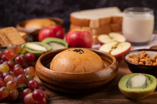 O café da manhã consiste em pão, maçãs, uvas e quivi em uma mesa de madeira. - Foto, Imagem