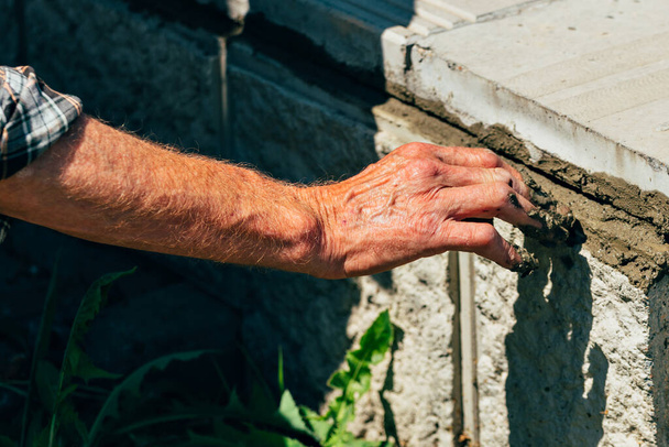 An old bricklayer lays out concrete tiles outside on a summer day. - Photo, Image