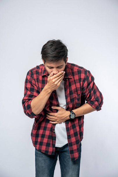 Um homem de pé com uma dor de estômago Coloque as mãos no estômago e cubra a boca. - Foto, Imagem