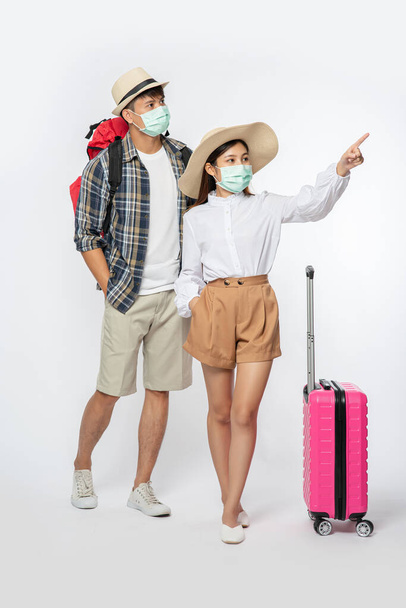 Men and women dressed to travel, wearing masks along with luggage. - Φωτογραφία, εικόνα