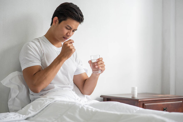 Un hombre que está enfermo en el sofá y está a punto de tomar antibióticos. - Foto, imagen