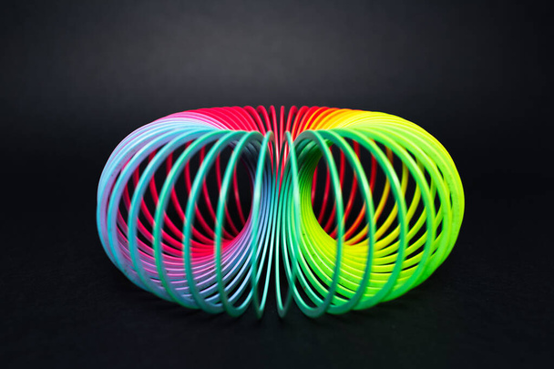 Bunte Regenbogenspirale Spielzeug zum Spielen auf schwarzem Hintergrund. - Foto, Bild