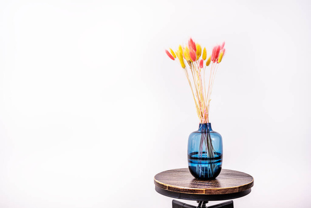 Jarrón de vidrio azul con plantas secas rojas y amarillas para decorar en interiores en taburetes industriales de madera y hierro - Foto, Imagen