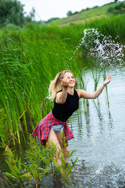 A menina loira está se divertindo no rio em botas de borracha no país. Jovem mulher em um lago desfrutar da vida. - Foto, Imagem