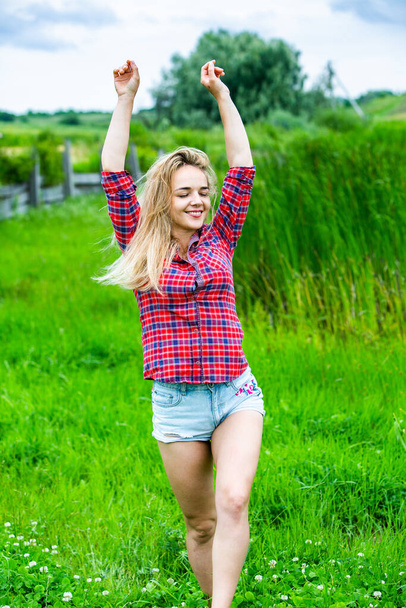 Het blonde meisje heeft plezier in de rivier met rubberen laarzen in het land. Jonge vrouw op een meer genieten van het leven. - Foto, afbeelding