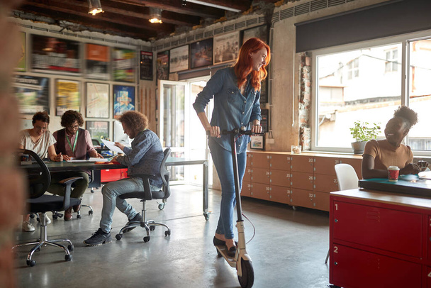 Une jeune femme s'amuse en scooter dans une ambiance détendue au bureau. Employés, bureau, travail - Photo, image