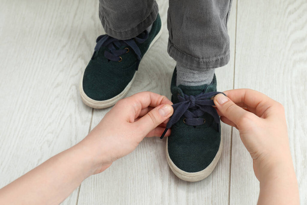 Mother helping son to tie shoe laces at home, closeup - Foto, Imagen