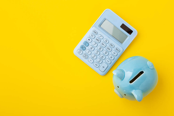 Piggy bank with calculator on yellow background, top view - Photo, Image