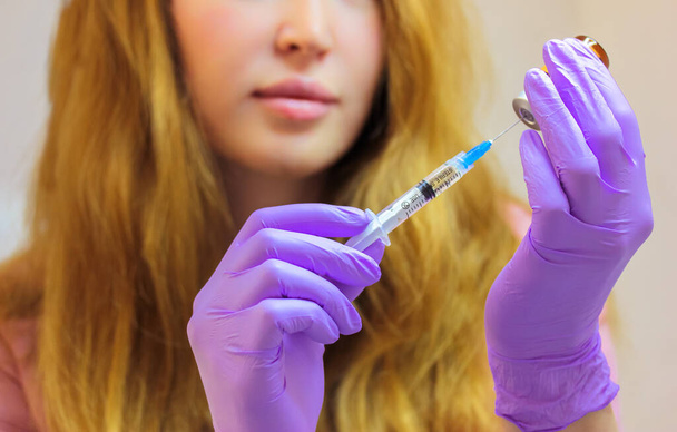 Uma jovem médica usando luvas de borracha roxa segura uma seringa para injetáveis com uma agulha fina. Procedimento de aumento labial, facial, rejuvenescimento corporal, mesoterapia. Cosmetologia estética. Salão de beleza - Foto, Imagem
