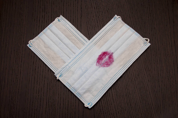 maska sanitarna z pocałunkiem z czerwoną szminką leży na ciemnobrązowym stole - Zdjęcie, obraz