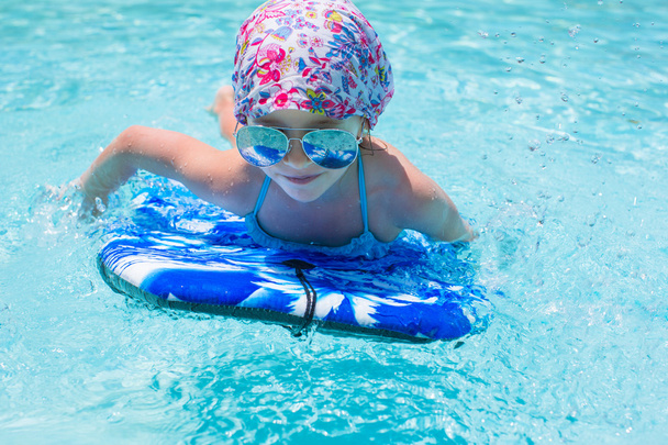 Petite fille nageant sur une planche de surf dans swimmingpoll
 - Photo, image