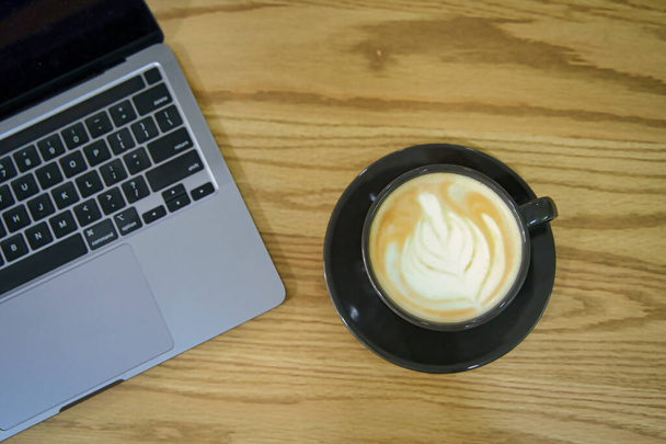 Une tasse de café et un ordinateur portable sur une table en bois rustique. Pause café. Latte art. Travaillez à la maison et prenez un concept de pause. Cuisine et maison. - Photo, image