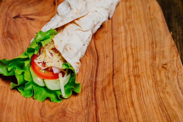 pita tortilla roll with vegetables and cheese on a wooden cutting board.  - 写真・画像