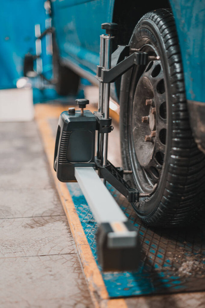 Primer plano de un neumático sujetado por un nivelador que pasa la alineación automática de las ruedas en el garaje, garaje y herramientas para el mecánico. nuevo - Foto, Imagen