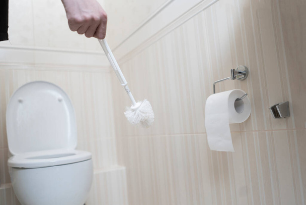 una mano sosteniendo un cepillo exfoliante y limpiando el inodoro - Foto, imagen