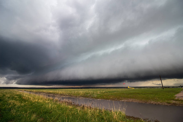 Eine Regalwolke nähert sich an der Spitze eines Sturms auf der großen Ebene, mit einem wassergefüllten Kanal im Vordergrund. - Foto, Bild