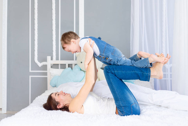 幸せで愛情のある家族。母親と赤ちゃんの息子はベッドの上で家で遊ぶ、楽しさと笑いを持っている - 写真・画像