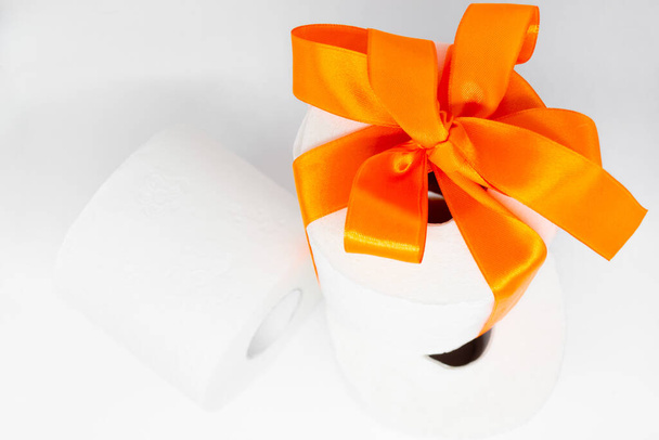Varios rollos de papel higiénico blanco perforado. Un rollo está atado con una cinta de satén naranja brillante como regalo. - Foto, imagen