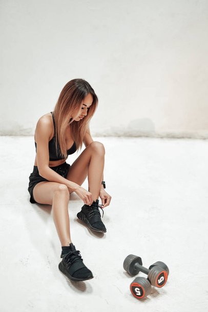 Sportlerin am Boden mit Hanteln schnürt Schnürsenkel - Foto, Bild