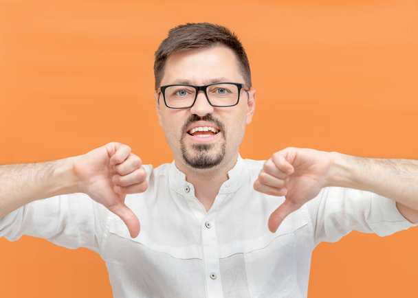 Angry annoyed bearded man in casual on yellow background unhappy shows a gesture of dislike with his hands, pointing two thumbs down looking at camera. Negative sign, rejection concept - Photo, Image