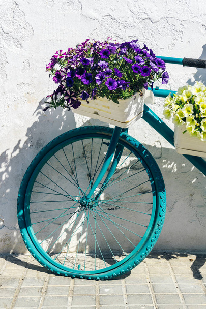 Kolo s květinovými košíky opřené o starou bílou stěnu - Fotografie, Obrázek