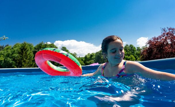 fille se baignant dans une piscine d'eau très bleue sourit avec son flotteur inséparable. - Photo, image