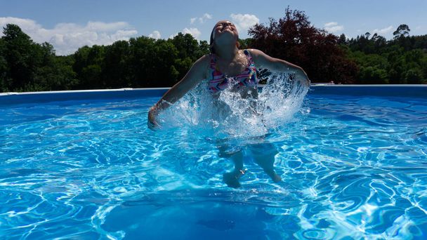 lány ugrás és élvezi a napsütéses nap úszás közben a medencében - Fotó, kép