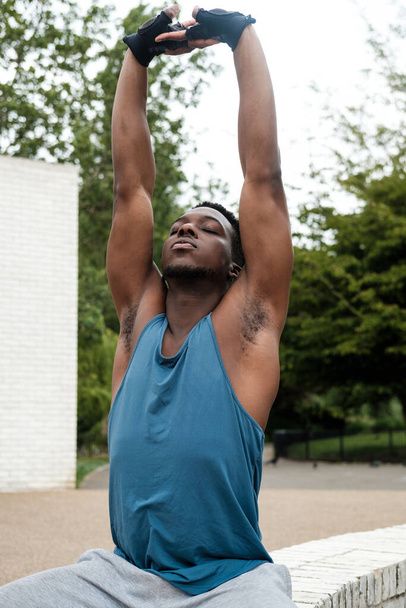Fit young black man stretching his arms. He is wearing a blue sleeveless t-shirt. - Photo, Image