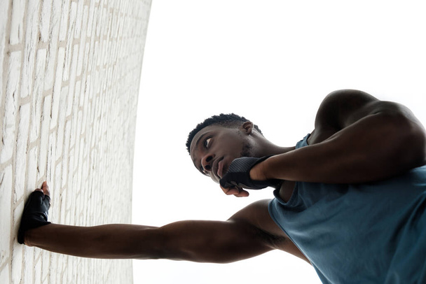 Fit young black man stretching against a brick wall.. He is wearing a blue sleeveless t-shirt. - Foto, imagen