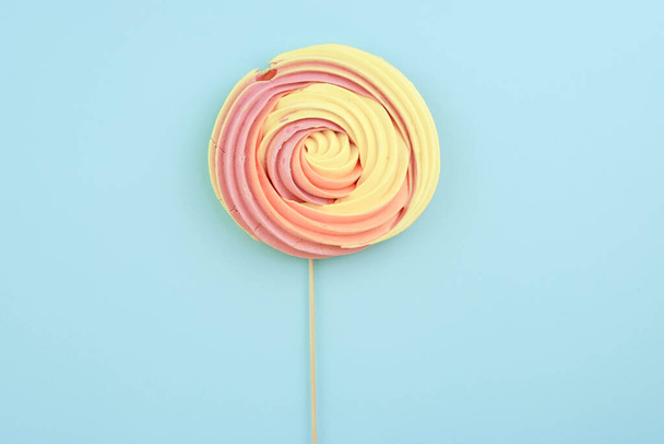 Meringue candy on a stick on a blue background. Round flat candy with a wooden stick top view.  - Foto, Imagen