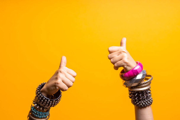 Hand gestures. Thumbs up, like approval. Two womens hands with lots of bracelets, youth fun style. - Фото, изображение