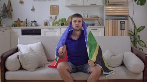 A white male sports fan watches TV at home with the South African flag - Footage, Video