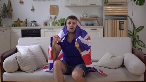 Mužský sportovní fanoušek britského národního týmu doma s vlajkou Spojeného království - Záběry, video