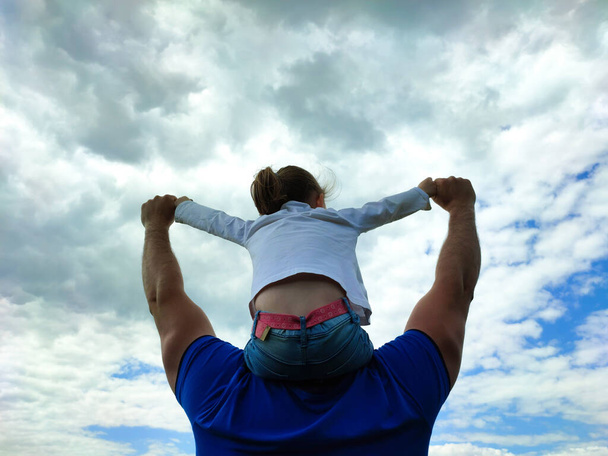 Vaderdag. Papa houdt zijn dochter op zijn schouders tegen de achtergrond van een groen veld van dichtbij - Foto, afbeelding