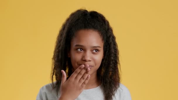 Schattig Afrikaans amerikaans meisje tiener verzenden blow kiss naar camera en glimlachen, gevoel verlegen over oranje achtergrond - Video