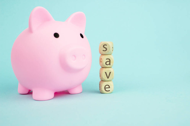 Pink piggy bank with geometric wood blocks cube adt text SAVE on blue background. Saving money concept - Photo, Image