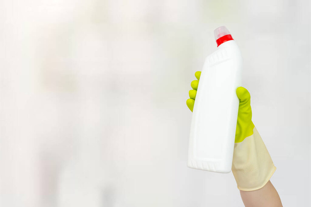 Voorjaarsschoonmaak concept. Witte fles met vloeibaar wasmiddel in de hand met gele rubberen handschoenen. Het begrip schoonmaakdienst - Foto, afbeelding