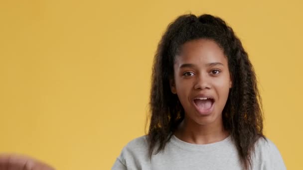 Pozitif Afro-Amerikalı genç kız iyi niyet gösteriyor ve turuncu stüdyo arka planında boş alan olduğunu söylüyor. - Video, Çekim