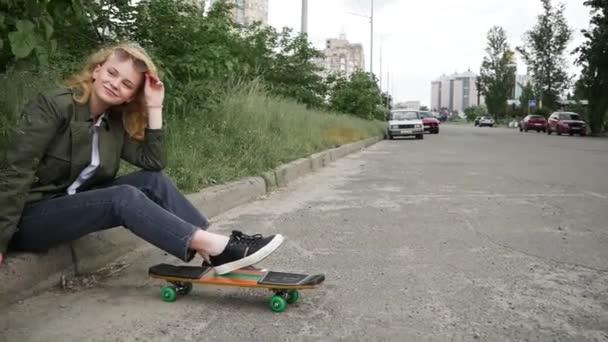 Ragazza adolescente con uno skateboard seduto sul marciapiede - Filmati, video