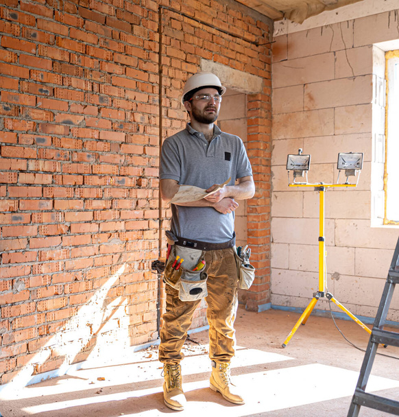 Ein Bauarbeiter in Arbeitskleidung begutachtet eine Bauzeichnung auf einer Baustelle. - Foto, Bild