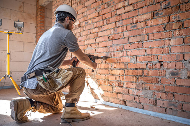 Egy építkezésen dolgozó ezermester a fal perforátorral történő fúrásának folyamatában. - Fotó, kép