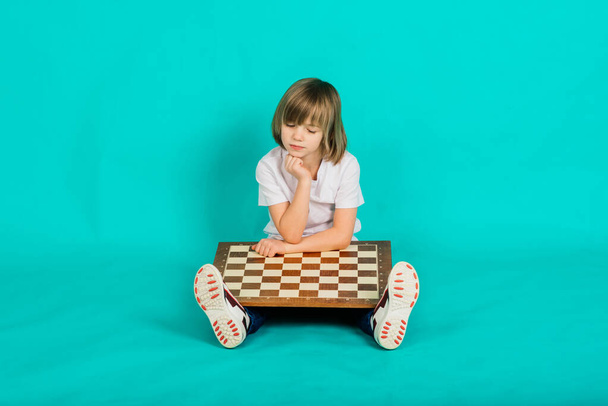 Çocuk elinde bir satranç tahtası tutuyor ve ona bakıyor, duygusal pozlar veriyor. - Fotoğraf, Görsel