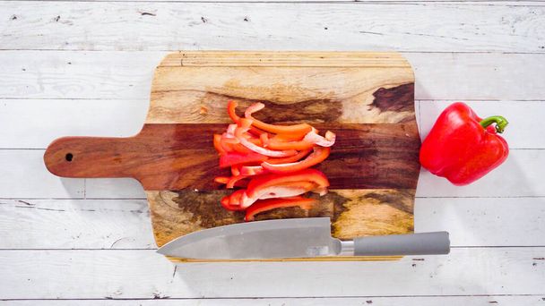 Flat lay. Mincing organic red bell peppers on a wood cutting board. - Φωτογραφία, εικόνα
