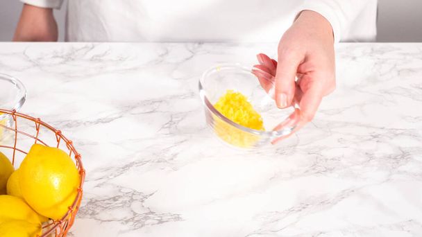 Paso a paso. Zesting limones frescos en un recipiente de mezcla de vidrio para preparar pastel de paquete de limón. - Foto, imagen