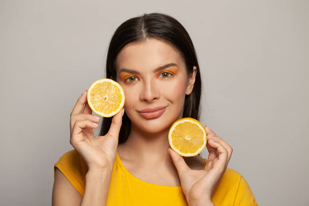 Barátságos fiatal nő tiszta bőr és egyenes haj gazdaság citrom gyümölcsök fehér háttér - Fotó, kép
