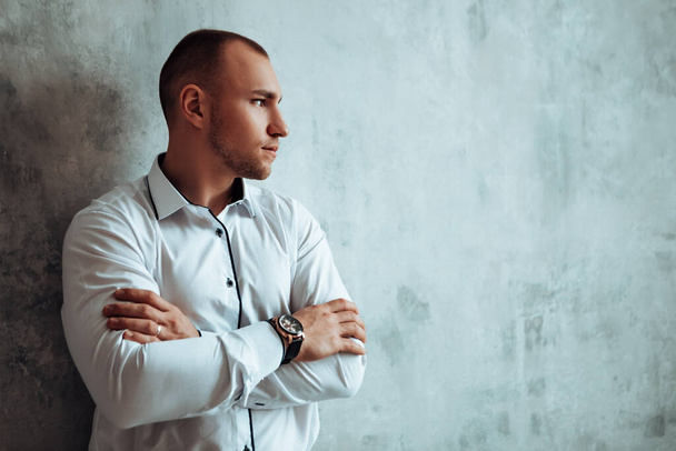 Man standing near concrete wall crossed arms watches on wrist looking away thinking. Groom dressed wear white shirt official photoshoot marriage day wedding ring on finger, luxury copyspace - Foto, immagini