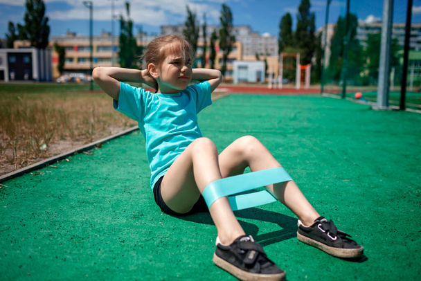 Chica preadolescente haciendo ejercicios con banda de resistencia a la aptitud en el campo deportivo público en la ciudad, deporte - Foto, Imagen