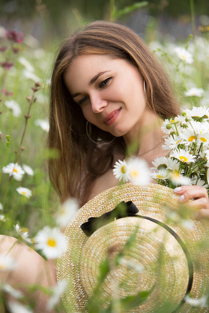 Retrato de una joven hermosa mujer con un sombrero de paja con un ramo de margaritas en el campo. - Foto, imagen