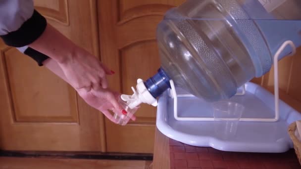 Chica vierte agua de un refrigerador en un vaso de plástico, las manos femeninas vierten agua de un refrigerador - Imágenes, Vídeo