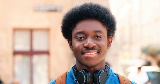 Portrait of young African American guy of multiracial ethnicity with headphones standing on the warm spring city street dressed at the casual clothes during morning. - Fotografie, Obrázek